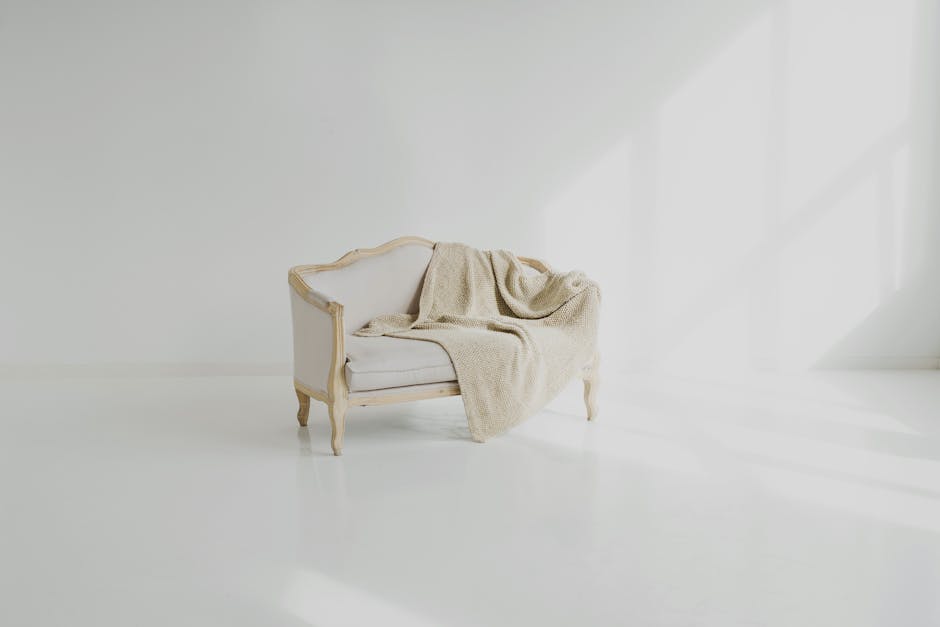 A person using a handheld upholstery cleaning tool connected to a vacuum or steam cleaning device to deep clean a beige fabric car seat, focusing on removing dirt and stains from the textured upholste